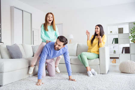 Photo portrait of parents playing with small daughter sitting piggyback on daddy at home