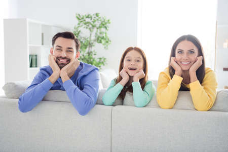 Photo of cheerful family mom dad child happy positive toothy smile hands touch cheeks sit sofa home weekendの写真素材