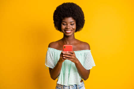 Photo portrait of girl holding phone in two hands texting isolated on vivid yellow colored backgroundの写真素材