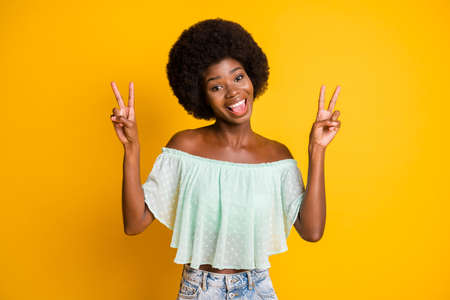 Photo portrait of funny girl showing two v-signs isolated on vivid yellow colored backgroundの写真素材