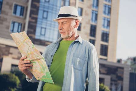 Photo of attractive confident mature man wear jeans shirt headwear walking looking map outside urban city streetの写真素材