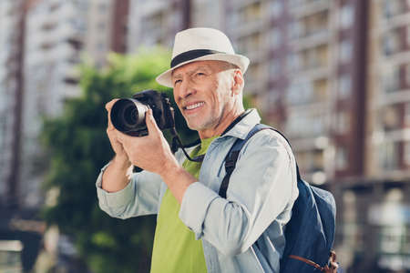 Photo of handsome mature man wear jeans shirt headwear rucksack tacking photo modern camera outside urban city streetの写真素材