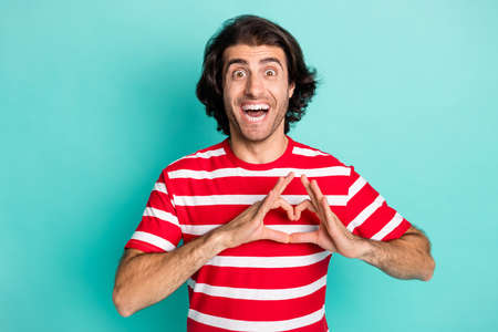 Portrait of handsome amazed cheerful guy showing heart shape isolated over bright green turquoise color backgroundの写真素材