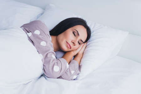Photo of pretty charming young woman nightwear lying pillow closed eyes hands cheek inside indoors home roomの写真素材