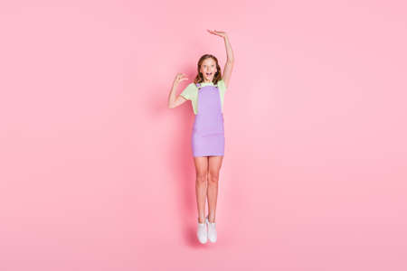 Full length body size photo of amazed small girl jumping high showing little big size isolated pastel pink color backgroundの写真素材