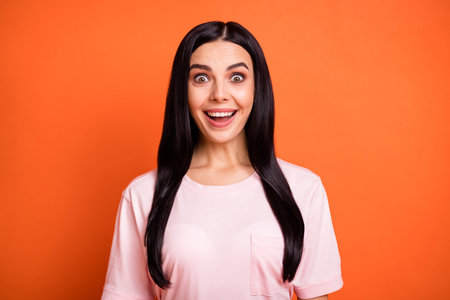 Portrait of shocked young lady open mouth smile look camera cant believe isolated on orange color backgroundの写真素材