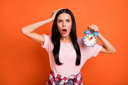 Portrait of impressed sad brunette lady hold clock hand head wear pink t-shirt isolated on orange...