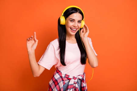 Portrait of optimistic nice brunette lady listen music sing wear headphones pink t-shirt isolated on orange color backgroundの写真素材