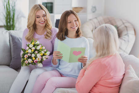 Photo of grey haired old woman little girl and family sit sofa read card flowers celebrate 8-march...