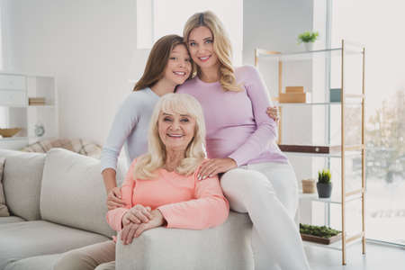 Photo portrait of happy female relatives having family time embracing sitting on sofa at home on weekends smilingの写真素材