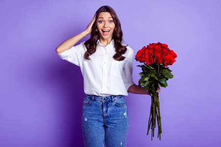 Photo of amazed cheerful lady hold red roses palm head wear white shirt isolated violet color...