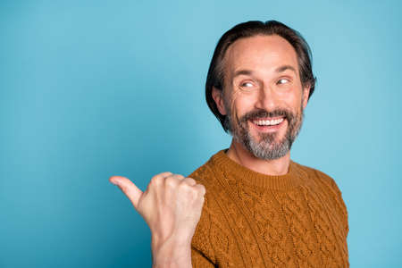 Portrait of mature handsome positive cheerful smiling man advertising point finger copyspace isolated on blue color backgroundの写真素材