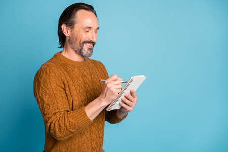 Profile portrait of positive friendly person arm hold pen notebook toothy smile isolated on blue color backgroundの写真素材