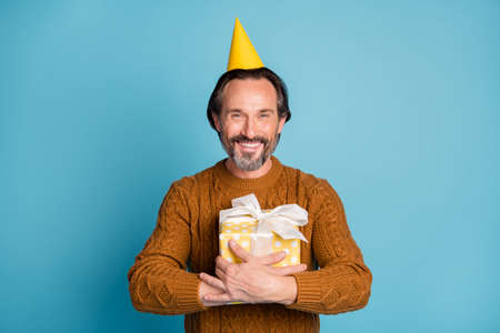 Photo portrait of cheerful smiling man wearing birthday yellow headwear embracing gift isolated on...