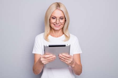 Photo portrait of old woman holding tablet in two hands wearing glasses isolated on grey colored...