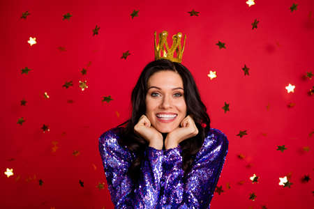 Photo of adorable pretty lady hold fists cheeks wear crown fall star confetti isolated on red color...