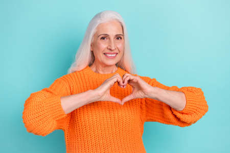 Portrait of attractive cheerful grey-haired woman showing heart sign affection isolated over teal...