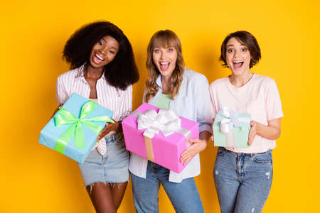 Portrait of three excited astonished ladies hands hold giftbox open mouth isolated on yellow color backgroundの写真素材