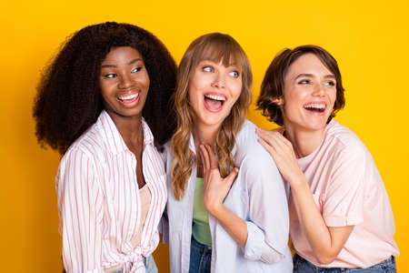 Photo of three carefree positive girls dark skin laughing look empty space isolated on yellow color...