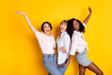 Portrait of three cheerful excited girls dark skin enjoy free time vacation disco isolated on yellow color backgroundの写真素材