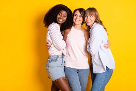 Portrait of three pretty cheerful persons hugging look empty space isolated on yellow color...