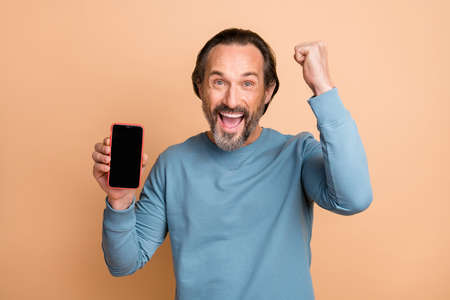 Photo portrait of middle-aged man showing smartphone display copyspace gesturing like winner...