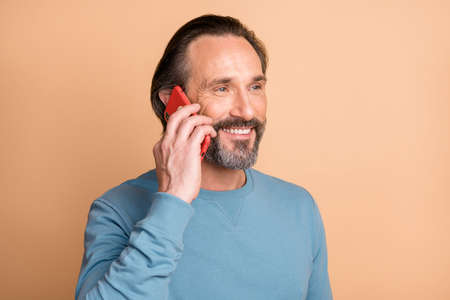 Photo portrait of mature man talking on phone isolated on pastel beige colored backgroundの写真素材