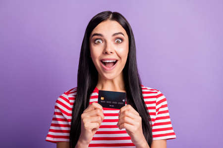 Photo of amazed happy crazy girl hold credit card spend savings isolated on purple color backgroundの写真素材