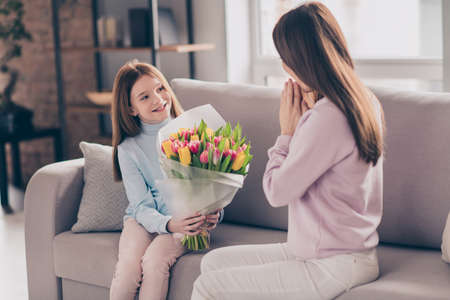 Photo of optimistic brunette red hairdo mom daughter take flowers sit on sofa wear sweater pants at homeの写真素材