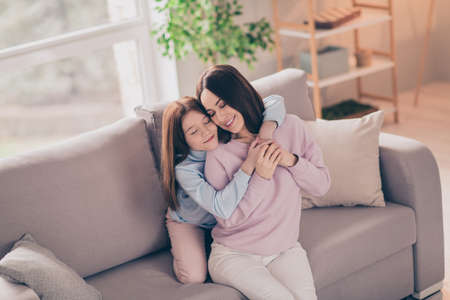 Photo of optimistic brunette red hairdo mom daughter hug closed eyes on sofa wear sweater at home