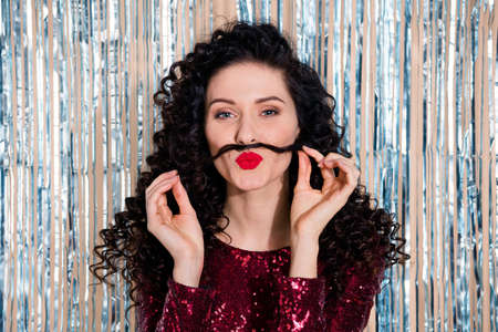 Photo of young beautiful funky attractive girl with fake mustache enjoying party isolated on glittered backgroundの写真素材