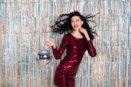 Photo of pretty positive girl hand hold disco ball look interested empty space toothy smile isolated on glossy backdropの写真素材