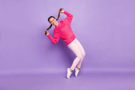 Full body photo of charming happy funky young woman hold braids dance isolated on purple color...
