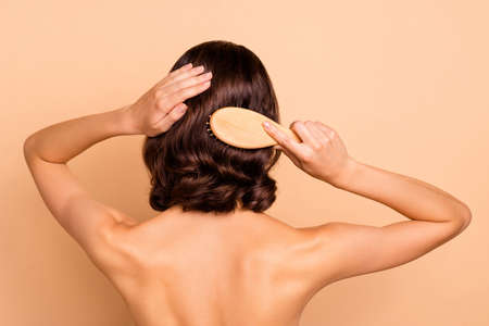 Close up back rear behind view photo beautiful lady brushing healthy brown curls ideal skin condition after visit new hair stylist hairdress wear no clothes isolated beige pastel backgroundの写真素材