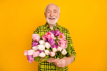 Photo of senior man hold bunch flowers smile wear checkered green shirt isolated yellow color backgroundの写真素材