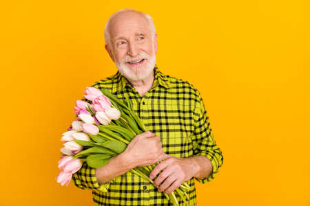 Photo of pensioner man hold bouquet flowers look empty space wear plaid green shirt isolated yellow color backgroundの写真素材