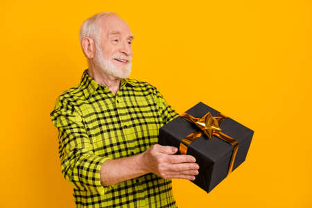 Profile side photo of old man happy positive smile give present box birthday party isolated over yellow color backgroundの写真素材