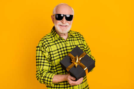 Photo of aged man happy positive smile hold gift box holiday wear sunglasses isolated over yellow...