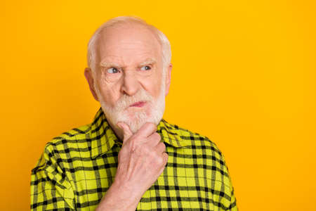 Photo of aged man pensioner unhappy hand touch chin serious think look empty space isolated over yellow color backgroundの写真素材