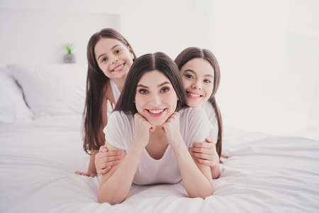 Photo of funky adorable three sisters sleepwear lying bed smiling hands arms chin inside indoors...
