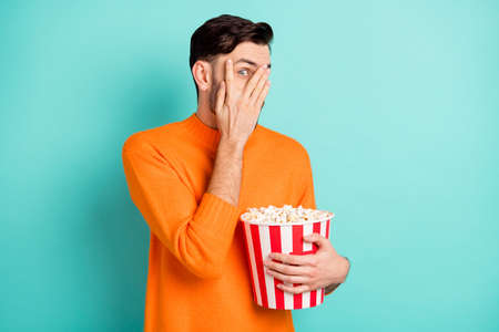 Photo of young guy close cover face hand hold popcorn box watch horror movie scared isolated over...