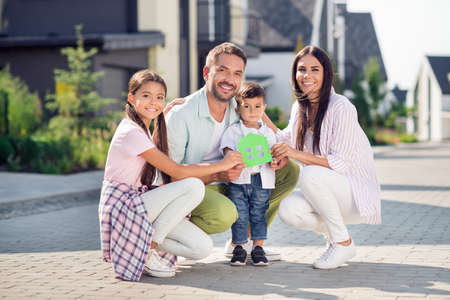 Full size photo of cheerful happy smiling family dad mom girl boy hold little green home card...