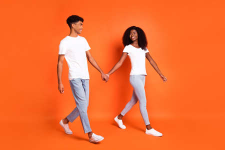 Full size profile side photo of young happy afro couple walking hold hands in love with each other isolated on orange color backgroundの写真素材