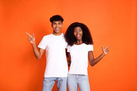 Photo of young smiling amazed afro couple hug each other pointing fingers copyspace isolated on orange color backgroundの写真素材