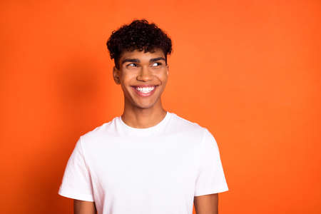 Photo of positive dark skin guy beaming smile look empty space thinking isolated on orange color backgroundの写真素材