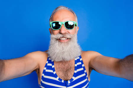 Photo of handsome positive smiling cheerful old man in sunglasses taking selfie isolated on blue color backgroundの写真素材