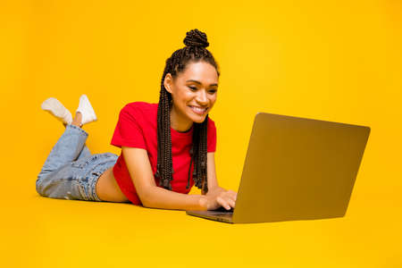 Profile side view portrait of lovely cheery girl lying using laptop typing blogging isolated on bright yellow color backgroundの写真素材