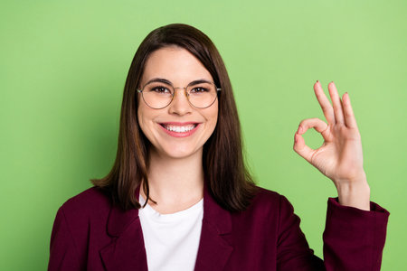 Photo of optimistic brown hairdo lady show okey wear spectacles red cardigan isolated on pastel green color backgroundの写真素材