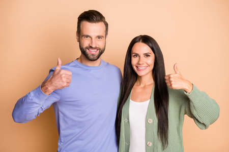 Photo of young happy cheerful smiling couple wife and husband showing thumb-up isolated on beige color backgroundの写真素材