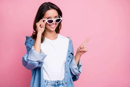 Photo of pretty cute woman hold sunglass point finger empty space isolated on pastel pink color...